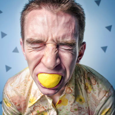 White man is sucking on a lemon. He is making a face that indicates the lemon is very sour.